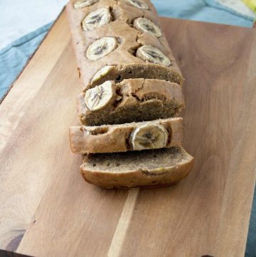 Banana bread on a wood cutting board and some bananas in the background