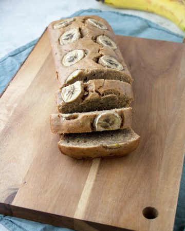 Banana bread on a wood cutting board and some bananas in the background